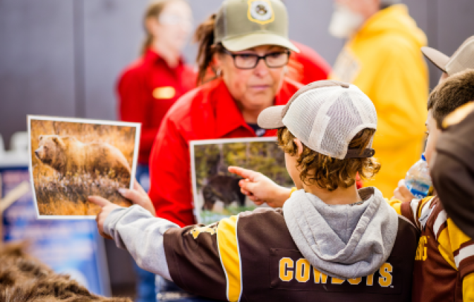 A Wyoming Game and Fish Department Employee ask a kid in a University of Wyoming Cowboys jersey to identify the type of bears shown on two different pieces of paper