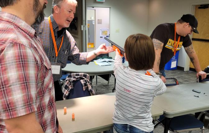 Student learning weapon safety during hunter's ed course with two instructors