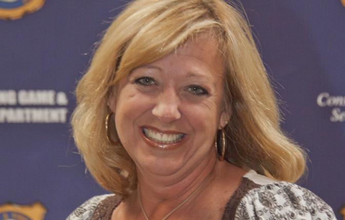 A woman smiles in front of a navy blue background 